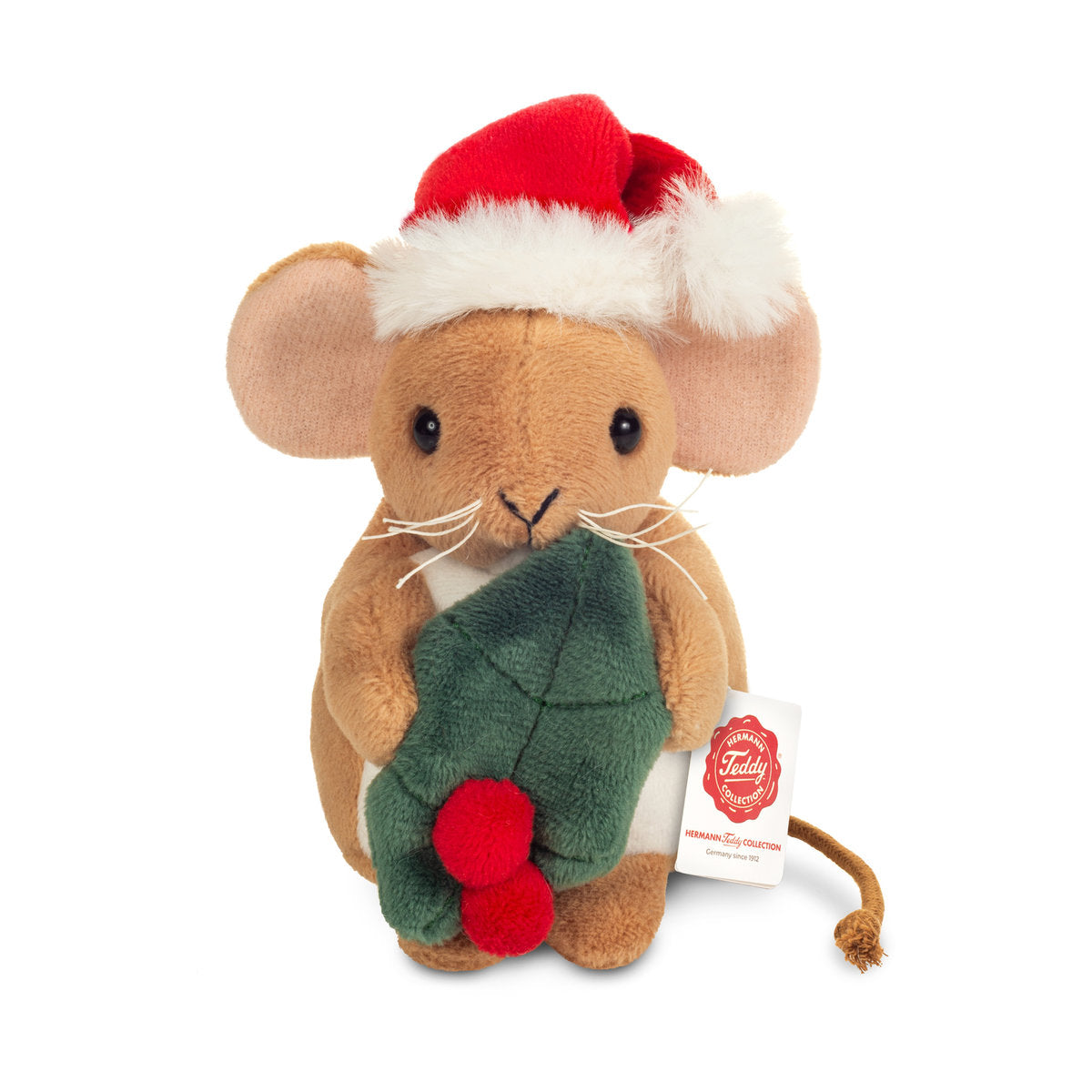 Det här är en julmus från Teddy-Hermann. Kort, slät och lätt blank beige päls, vit mage och ljusrosa insidor på öronen. Nosen är beige, ögonen svarta och runda, nosspetsen liten, svart och V-formad, med vita morrhår på var sida. Tassarna är beiga utan synliga trampdynor och svansen är ett tunt brunt snöre baktill. Musen sitter upprätt och håller ett grönt järneksblad med två röda runda bär och har en röd tomteluva med vit luddig kant och vit pompon. Minen är mild och nöjd.